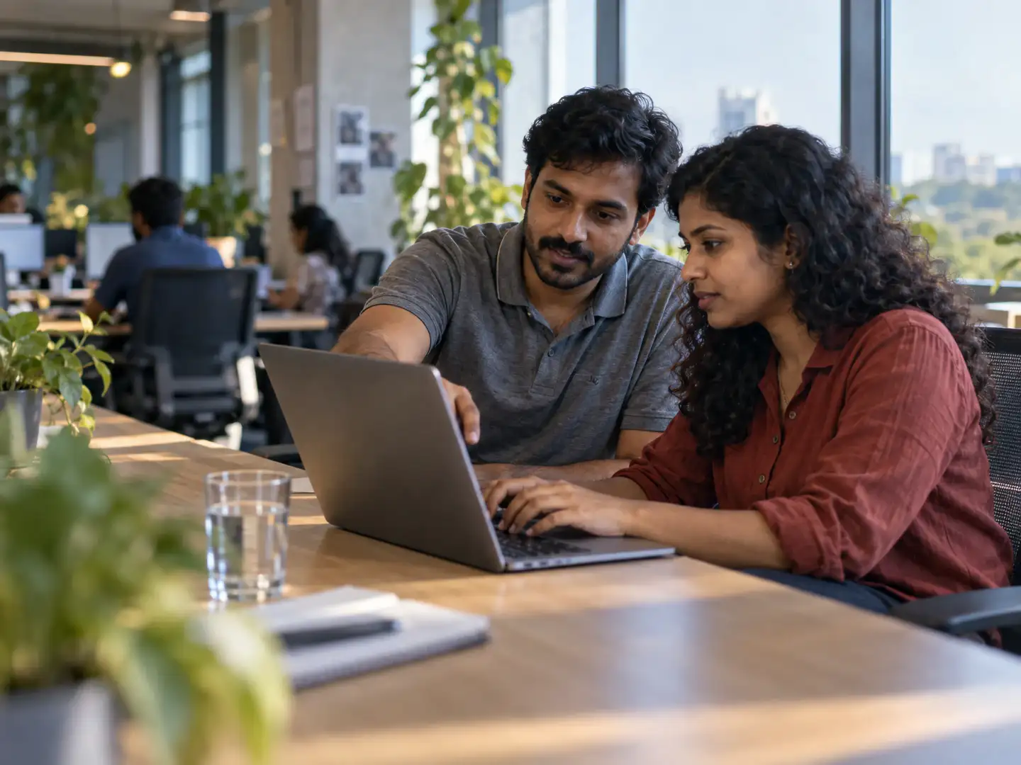 Two engineers working side by side at one desk, one pointing at the screen while the other types.